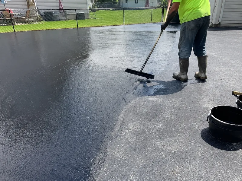 Worker applying black sealcoat to an asphalt driveway in Lafayette